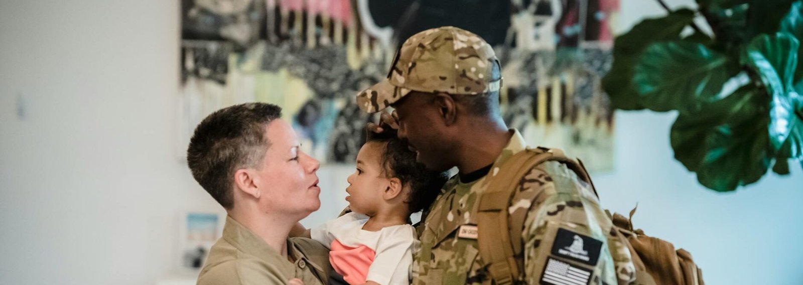 a woman carrying a child beside a man in military uniform